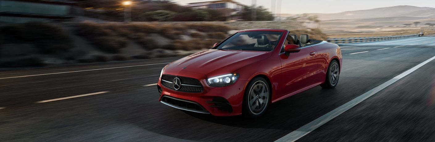 Side quarter view of a red 2022 Mercedes-Benz E-Class Cabriolet driving on a road
