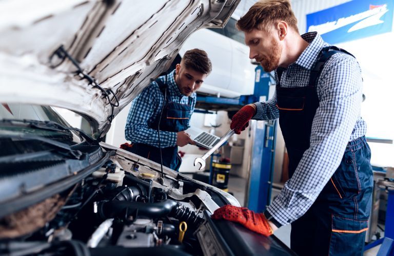 Two mechanics working under the hood of a vehicle