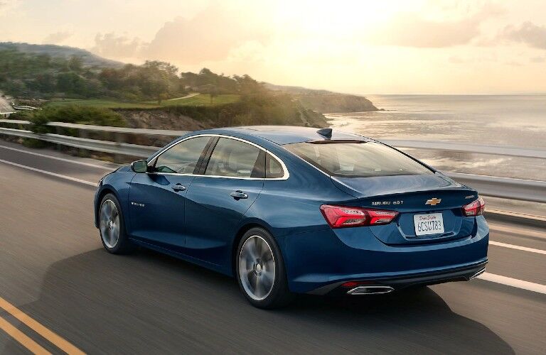 Rear driver angle of a blue 2020 Chevrolet Malibu driving near the ocean