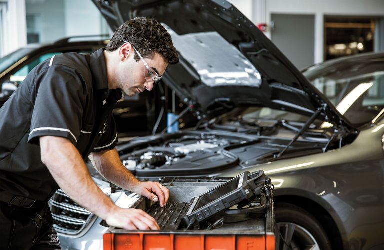 Mercedes-Benz mechanic leaning over computer in front of MB with open hood