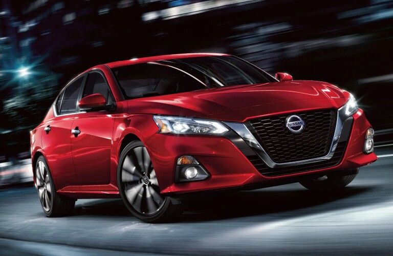 Front passenger angle of a red 2020 Nissan Altima driving at night through the city