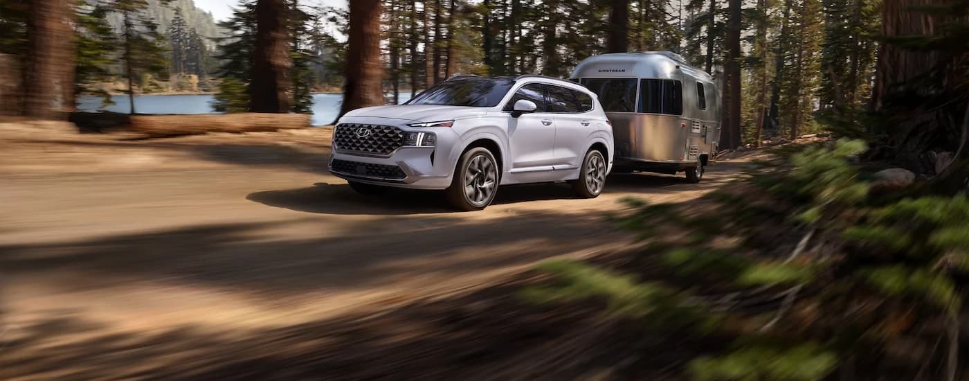 White 2023 Hyundai Santa Fe driving on a dirt road with a camper