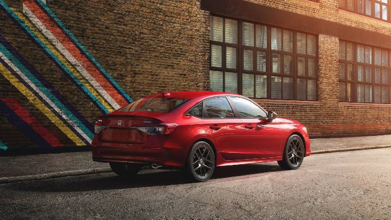 A rear 3/4 view of a red 2022 Mazda3 parked next to a brick building