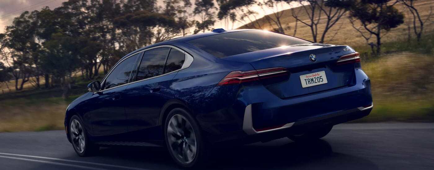 Blue 2026 BMW 5 Series driving down a road.