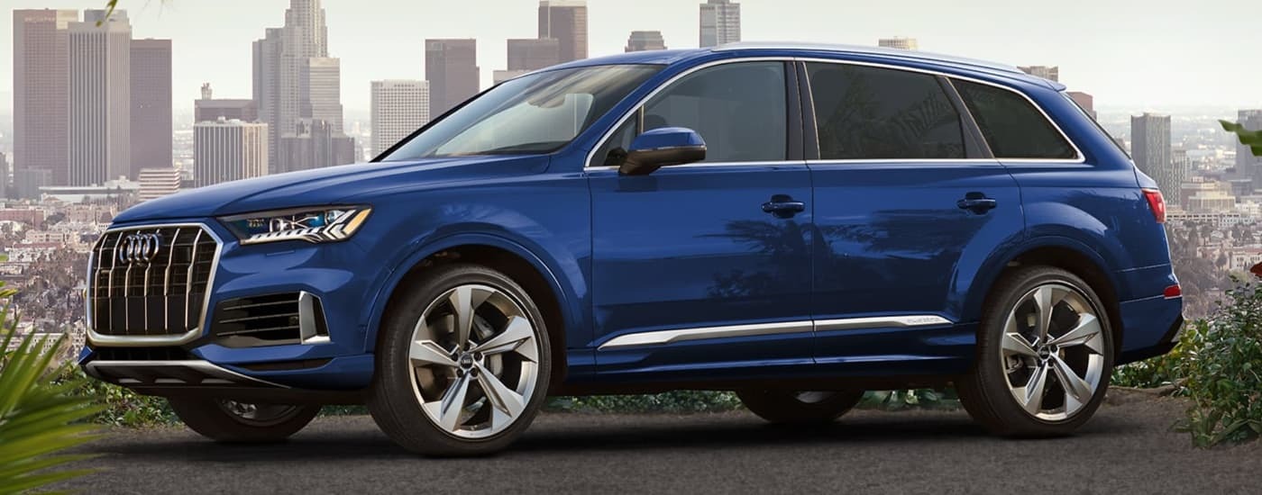 A blue 2022 Audi Q7 is parked on tar with a city view.