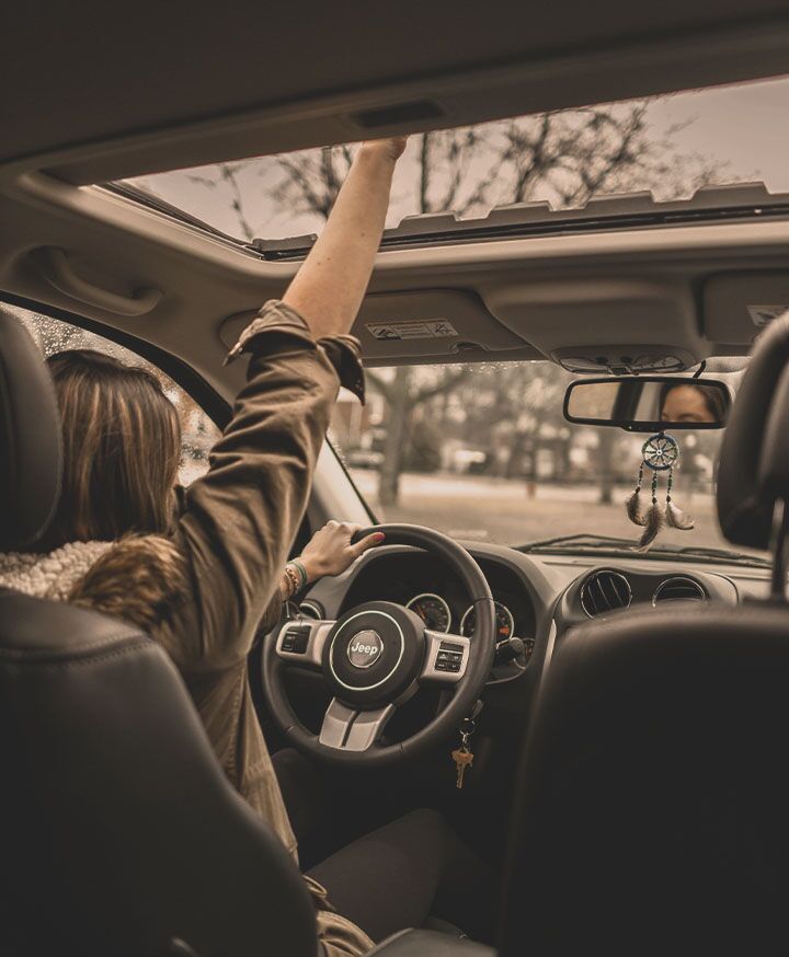 woman in driver seat with hand up through sun roof