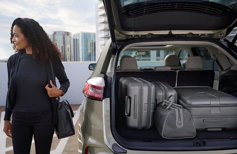 Rear angle of the 2020 Ford Edge with its liftgate open and luggage bags loaded inside and a woman standing next to it