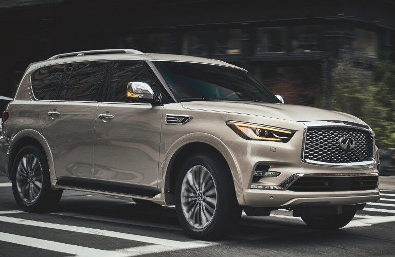 Front passenger angle of a tan 2021 INFINITI QX80 driving in a city