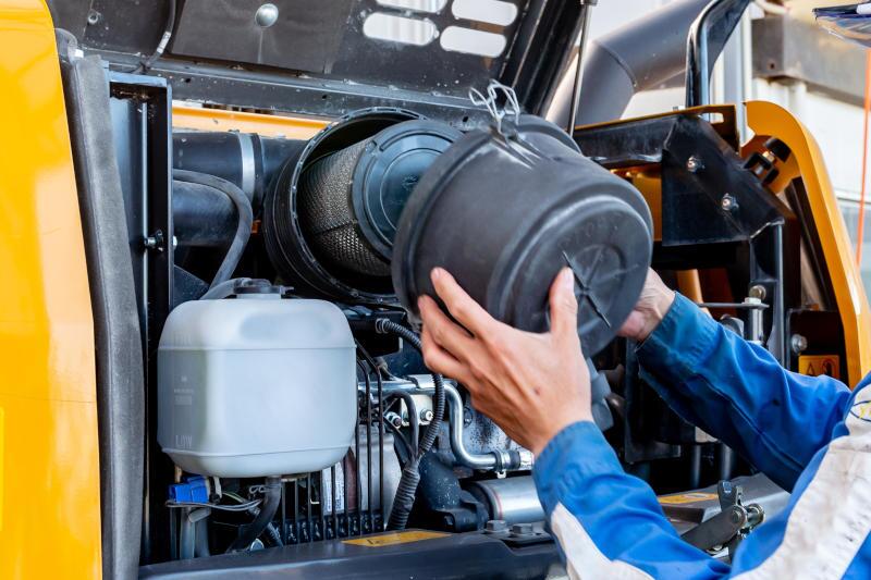 A man replacing an oil filter in a heavy truck, making sure to use the best parts available.