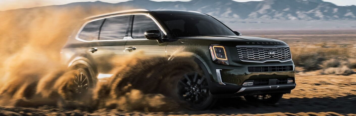 Exterior view of a green 2020 Kia Telluride spitting up sand while driving through the desert