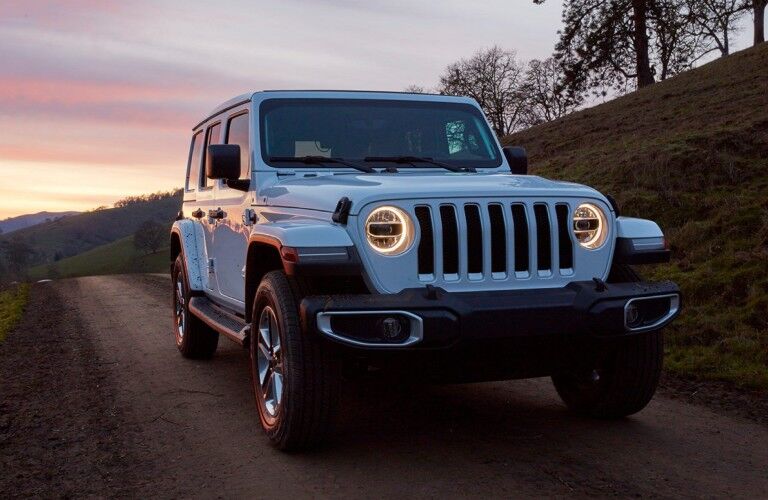 Front passenger angle of a white 2020 Jeep Wrangler driving on a trail with a sunset in the background