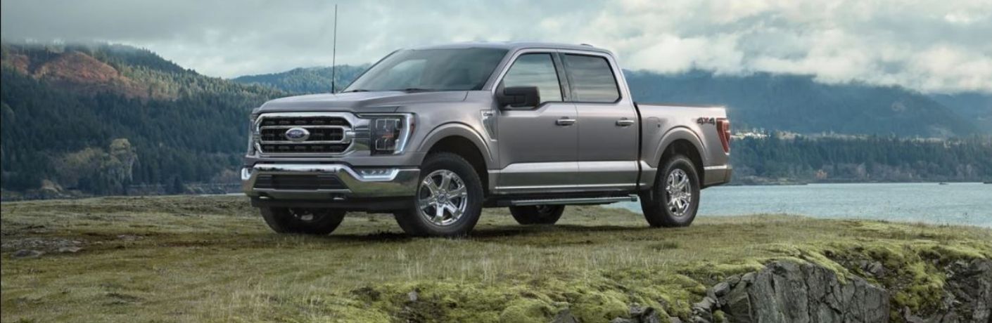 Side view of a grey 2021 Ford F-150 pickup truck parked on a cliff overlooking a lake