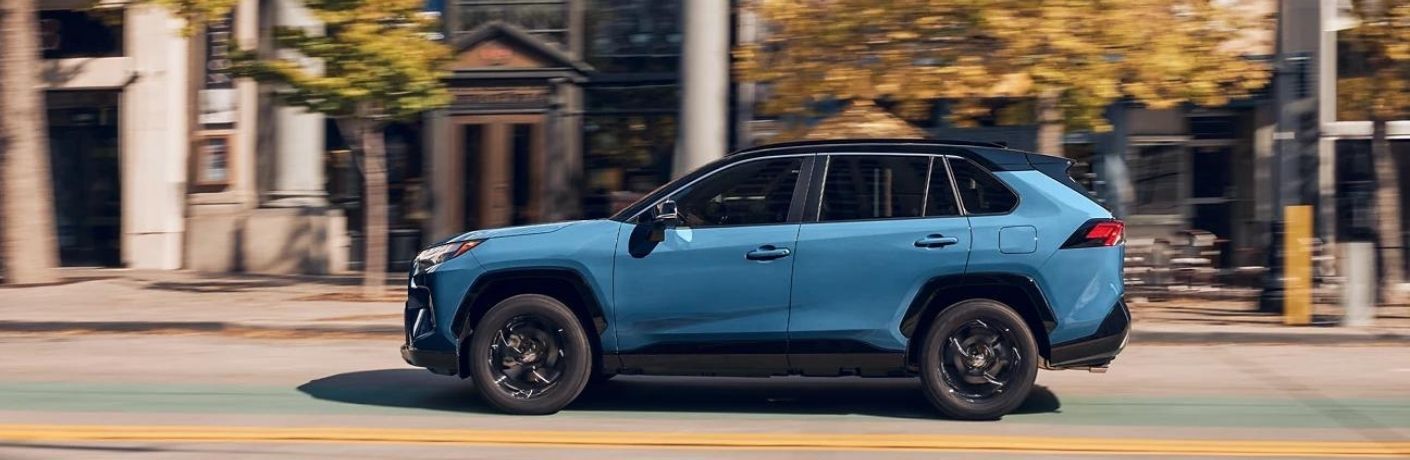 Side profile of a blue 2022 Toyota RAV4 Hybrid driving in the city.