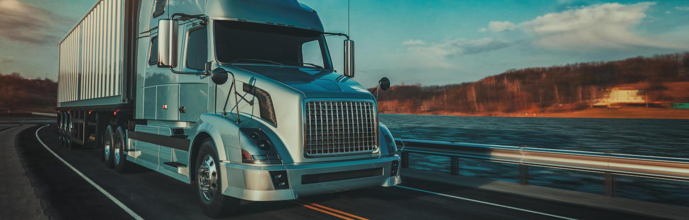 A heavy truck driving along a highway next to a river.