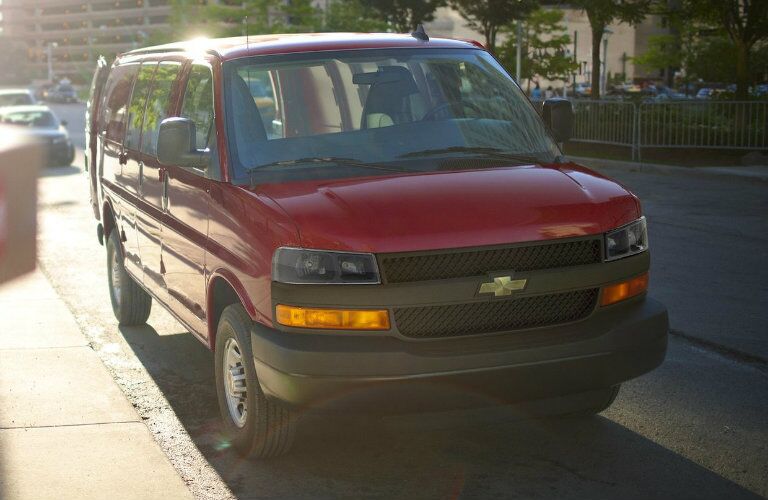 front view of red 2018 chevrolet express cargo van parked on curb of city sidewalk