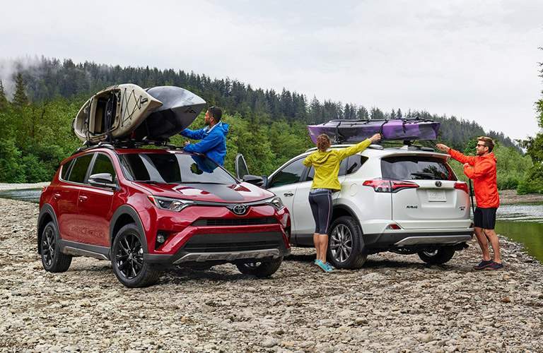 Two 2018 Toyota RAV4 Hybrid models parked on a rocky beach with kayaks on the roof rails