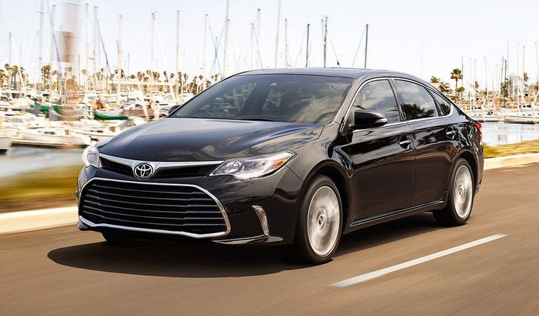 dark Toyota Avalon driving in front of a harbor
