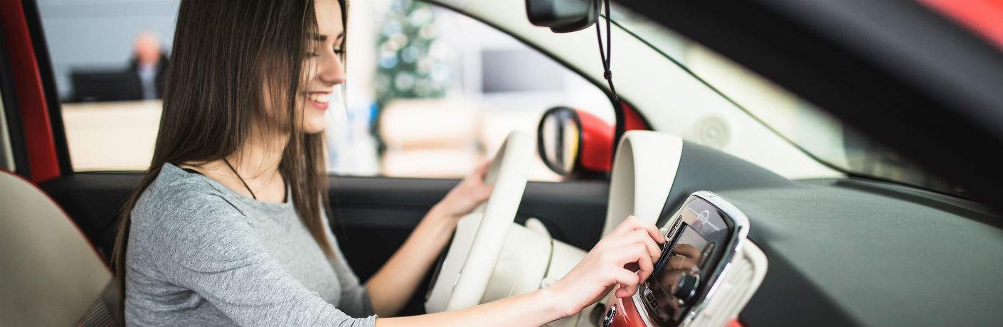 smiling brown-haired woman using car stereo in subcompact vehicle