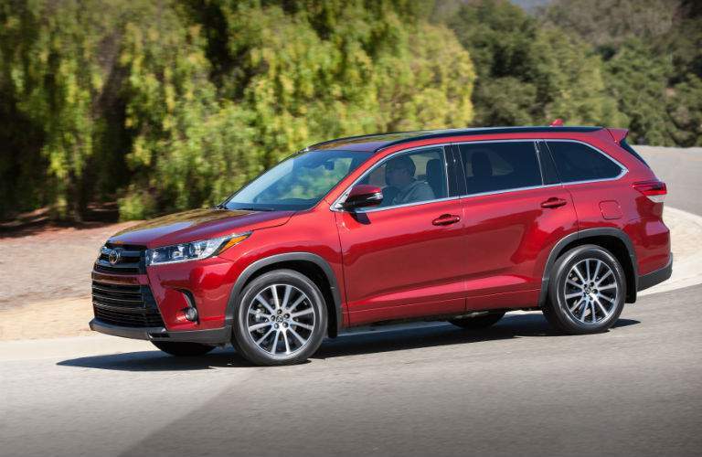 A left profile view of a red 2018 Toyota Highlander parked in front of some trees