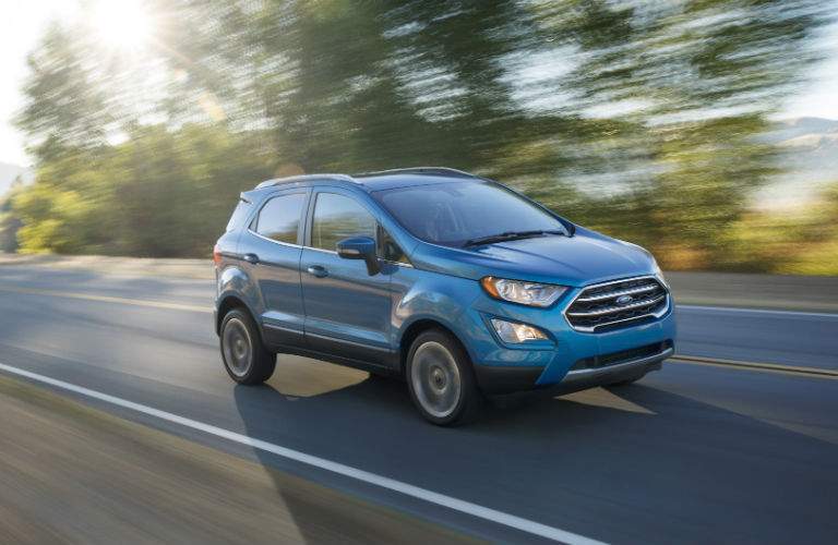 A right profile view of a light blue 2018 Ford EcoSport driving on a country road.
