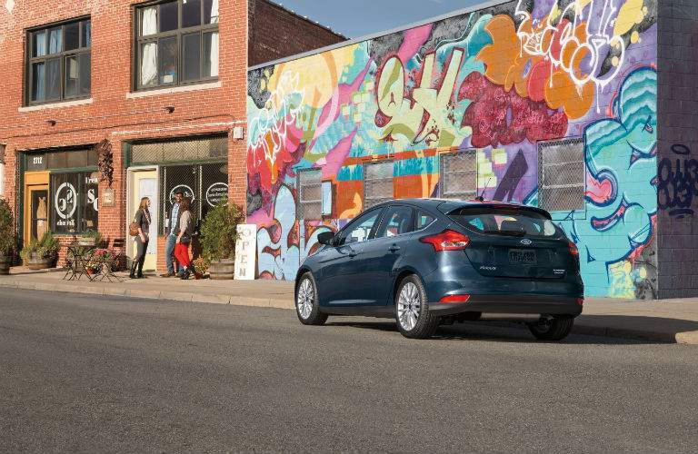 A rear quarter view of the dark blue 2018 Ford Focus hatchback in front of a mural