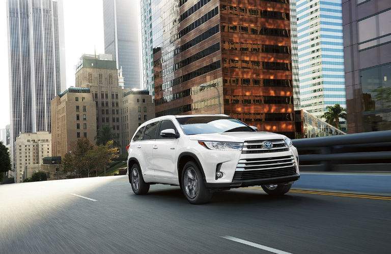 A front quarter image of a white 2018 Toyota Highlander driving through an urban setting