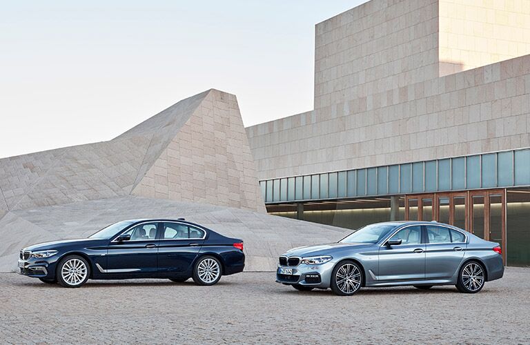 two 2017 BMW 5 Series sedans parked in front of a modernist sand-colored house
