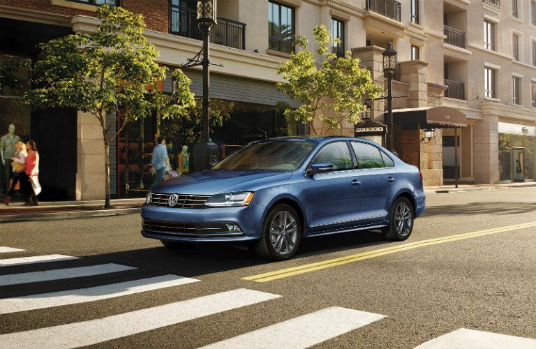 Long view of blue 2018 Volkswagen Jetta parked in front of tree-lined building