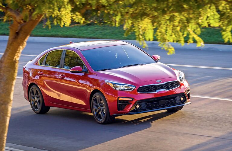 2019 Kia Forte exterior shot with red color paint job driving through a suburban neighborhood under tree shade