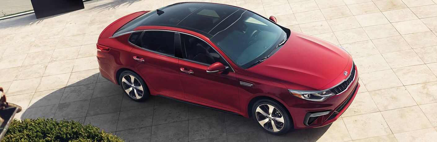 2019 Kia Optima overhead exterior shot with red paint color parked on a stone-tiled plaza