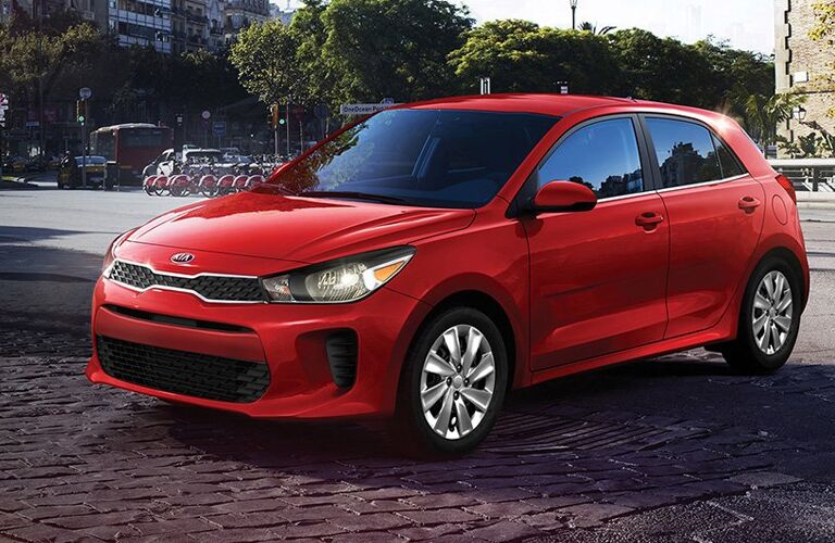 2019 Kia Rio hatchback exterior shot with red paint color parked on a stone tile road outside