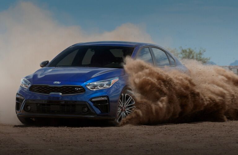 2020 Kia Forte GT exterior shot with blue paint color driving through sand and kicking up clouds of dust