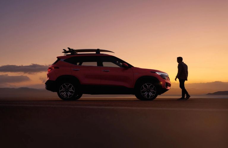 2021 Kia Seltos exterior side shot with red paint color parked in a sand dune at sunset