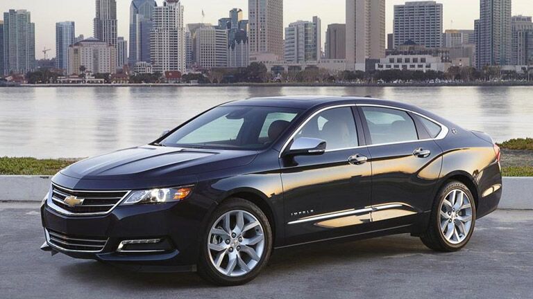 black 2015 Chevy Impala in front of a lake and a city