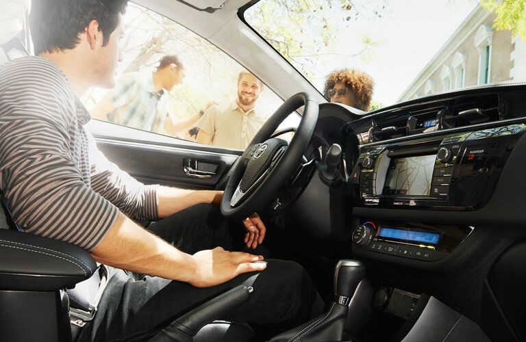 Man sitting in driver seat of 2017 Toyota Corolla looking out the window at friends