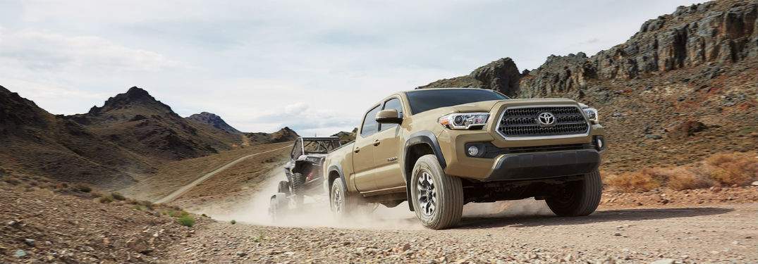beige 2017 toyota tacoma hauling 4-wheeler through desert road