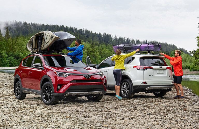 red and white 2018 toyota rav4 hybrids next to each other with mounted kayaks and young people around them