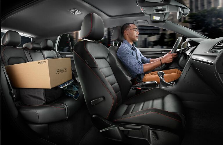 A man driving a 2019 Volkswagen Golf GTI with a box in the rear seat area