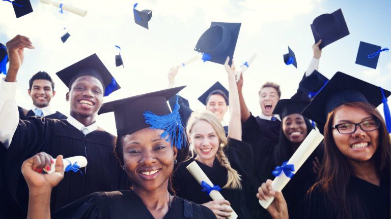 college graduates celebrating by throwing blue tassel graduation caps in the air