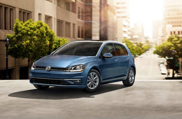 2019 Volkswagen Golf exterior shot with blue paint color driving through a suburban city neighborhood under the sun