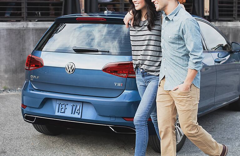 Two people walking by a blue 2019 Volkswagen Golf