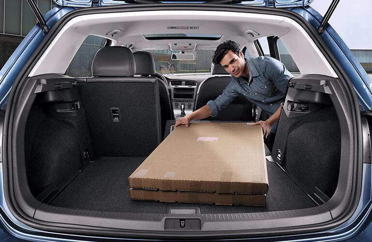 A man placing a box in the cargo area of a blue 2019 Volkswagen Golf
