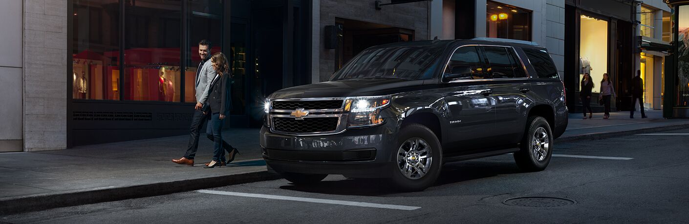 Two people walking past 2019 Chevrolet Tahoe parked on city street