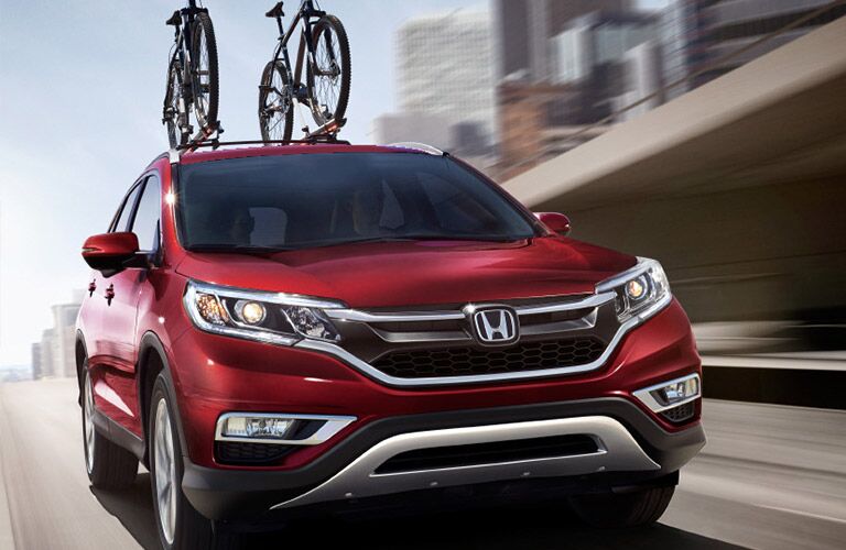 Red Honda CR-V cruises up a city highway with two bicycles standing proudly on its roof.