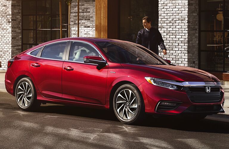 A man approaches a red Honda insight with a smile on his face.