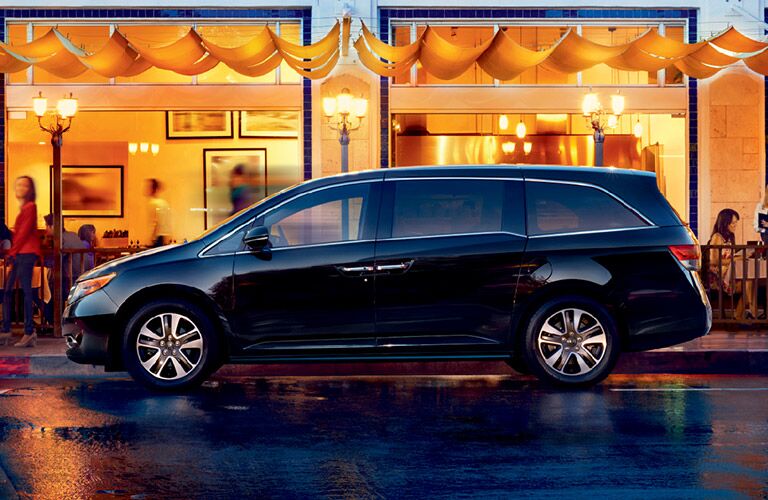 Black Honda Odyssey parked alongside a restaurant on a rainy night.