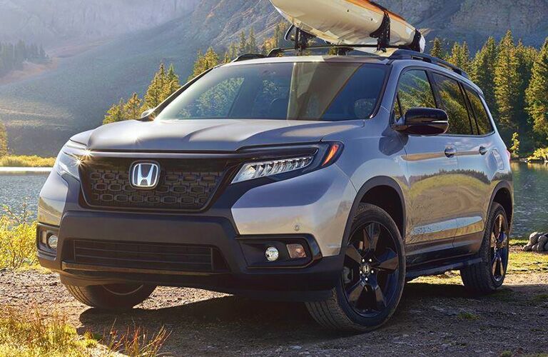 Reflective Honda Passport parked out in nature with a kayak on its roof.