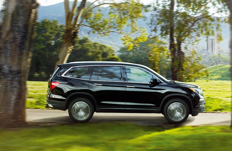 Black Honda Pilot ambles along a road in a park.