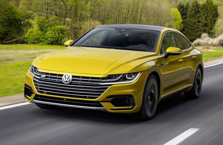 yellow Volkswagen Arteon driving by wooded area