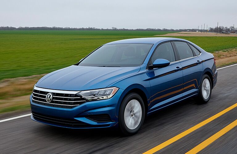 blue Volkswagen Jetta driving by farmland